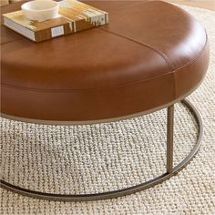 a brown leather ottoman sitting on top of a white rug next to a coffee table