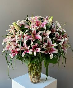 a vase filled with lots of pink flowers on top of a white table next to a gray wall