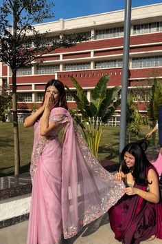 two women in pink saris are talking on their cell phones while another woman is holding her hand up to her ear