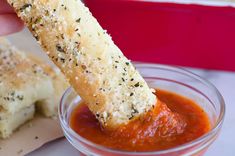 a person dipping some bread sticks into a small bowl of tomato sauce on the side