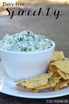 a white bowl filled with spinach dip surrounded by tortilla chips on a plate