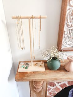 a wooden stand with jewelry on it next to a potted plant and a mirror