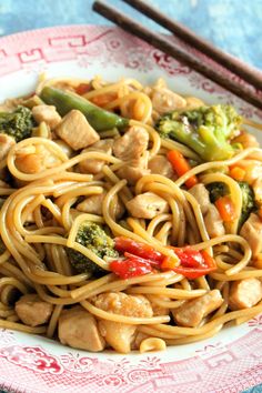 a plate full of noodles and chicken with chopsticks