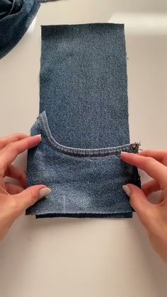 two hands are stitching together a piece of blue fabric with one end and the other end