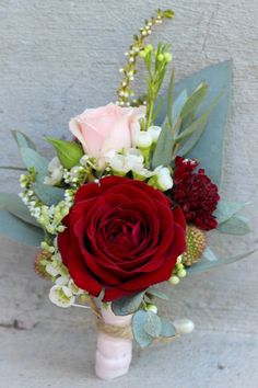 a bridal bouquet with red roses and greenery on the side of a wall