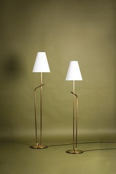 two floor lamps sitting next to each other on top of a green surface with a white lamp shade