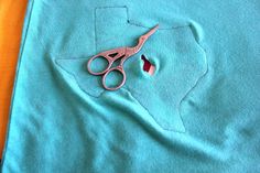 a pair of pink scissors sitting on top of a blue piece of cloth next to a hole in the fabric