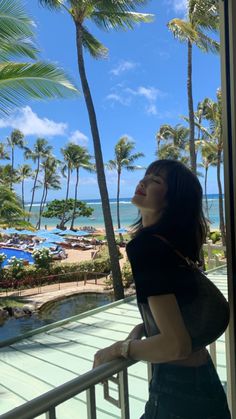 a woman standing on a balcony next to palm trees and looking up at the sky