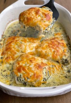 a casserole dish with spinach and cheese being scooped from the casserole