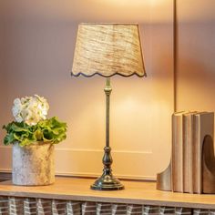 a lamp on a table next to books and a vase with white flowers in it