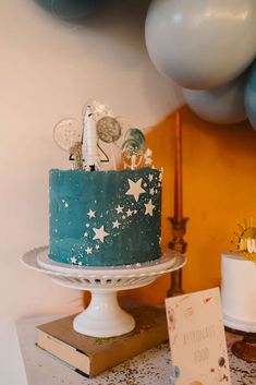 a blue cake with stars on it sitting on top of a table next to balloons