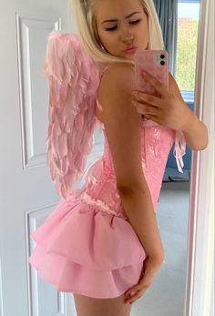 a woman taking a selfie with her cell phone wearing a pink dress and angel wings