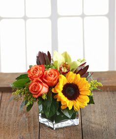 a vase filled with orange and yellow flowers on top of a wooden table next to a window