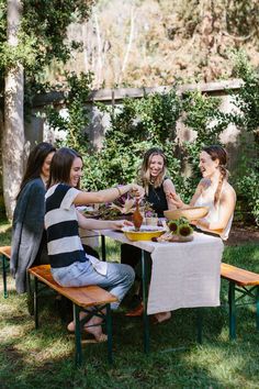 four women sitting at a picnic table with food