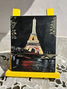 a painting of the eiffel tower is shown on a small easel that sits on a table