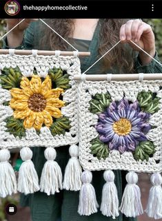 a woman holding up two crocheted wall hangings with tassels and flowers on them