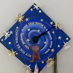 a blue graduation cap with gold stars and a hand pointing at the clock on it