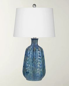 a blue vase lamp with a white shade on the base and a light in front of it