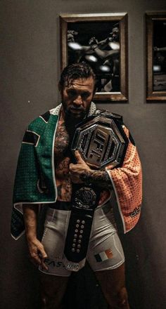 a man holding a wrestling belt in front of two pictures on the wall behind him