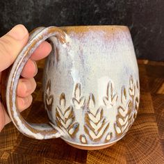 a hand holding a coffee mug on top of a wooden table next to a piece of wood