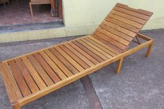 a wooden chaise lounge chair sitting on the concrete ground next to a yellow building