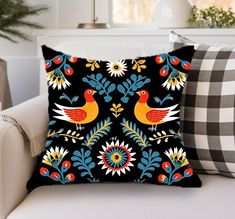 a black pillow with colorful birds on it sitting on a white couch next to pillows