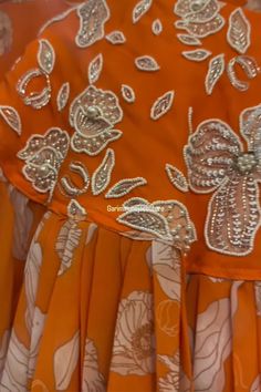 an orange dress with white flowers and silver sequins on the bottom, is shown in close up