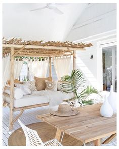 an outdoor living area with white furniture and wooden table, chairs, and canopy bed