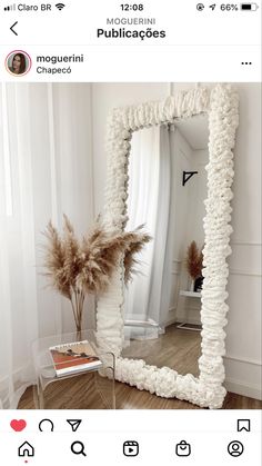 a large white mirror sitting on top of a wooden floor next to a vase filled with flowers