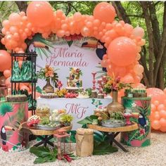 an outdoor dessert table with orange balloons and tropical themed decorations on the top, surrounded by palm trees