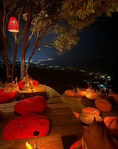 people are sitting on red bean bags outside at night with the city lights in the background