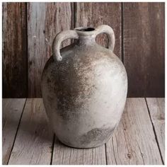 an old white vase sitting on top of a wooden table next to a wood wall