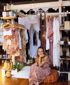 a woman sitting on the floor in front of a rack of clothes and other items