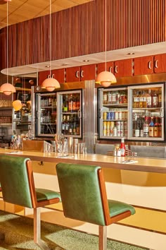 an empty bar with several bottles and glasses on the counter, along with two green chairs