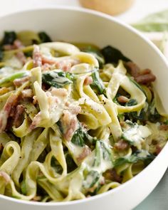 a white bowl filled with pasta covered in ham and spinach sauce on top of a table