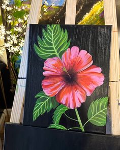 a painting of a pink flower with green leaves on a wooden easel next to other paintings