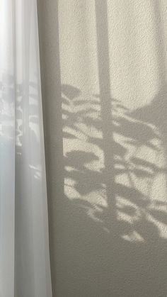 the shadow of a clock on a wall next to a window with white curtains in it