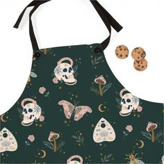 an apron with skulls and flowers on it, next to two cookies in the shape of mushrooms