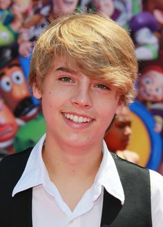 a young boy with blonde hair wearing a black vest and white shirt smiling at the camera