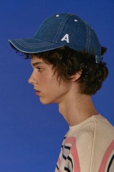 a young man with curly hair wearing a baseball cap on his head, against a blue background