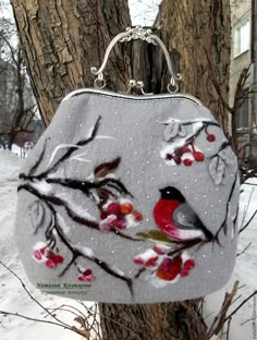 a handbag hanging from a tree in the snow with birds and berries on it