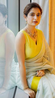 a woman in a yellow and white dress sitting next to another woman wearing a necklace