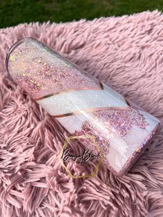 a pink and white bottle with glitter on it sitting on top of a pink blanket