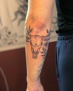 a person with a cow skull tattoo on their arm and leg, standing in front of a wall