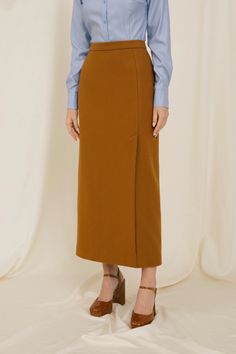 a woman standing in front of a white backdrop wearing a blue shirt and brown skirt