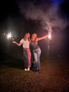 two girls are holding sparklers in their hands and posing for the camera at night