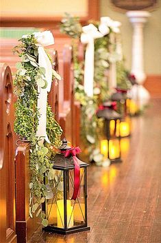 candles are lined up on the pews in front of an aisle decorated with greenery