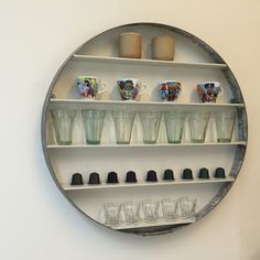 a round metal shelf filled with cups and glasses on top of a wall next to a white wall