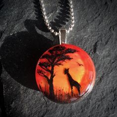 a glass pendant with a giraffe and tree on it sitting on a rock