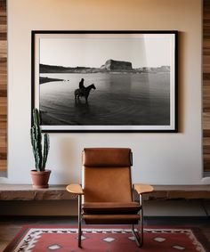 a black and white photo of a person on a horse in the water with a cactus next to it